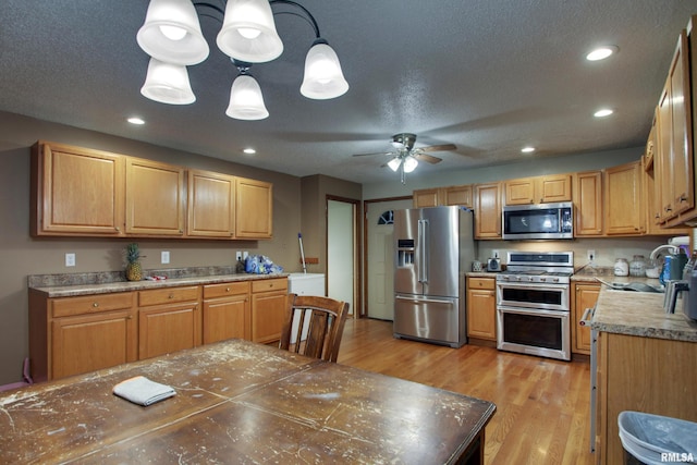 kitchen featuring stainless steel appliances, sink, ceiling fan, hanging light fixtures, and light wood-type flooring