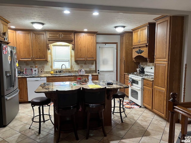 kitchen featuring backsplash, a kitchen bar, sink, white appliances, and a center island