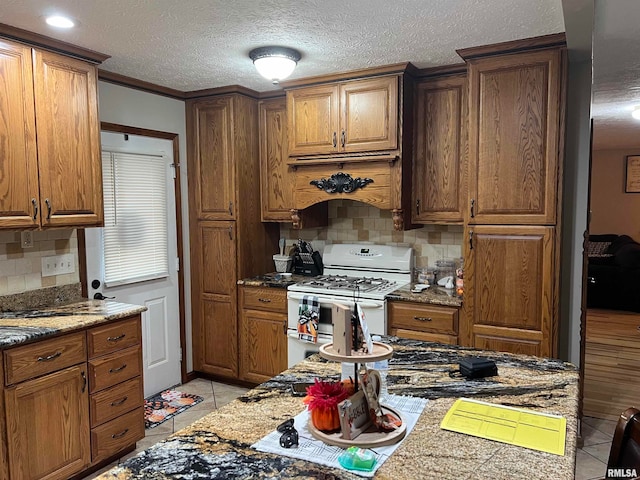 kitchen featuring white range with gas cooktop, light stone counters, light tile patterned floors, decorative backsplash, and custom exhaust hood