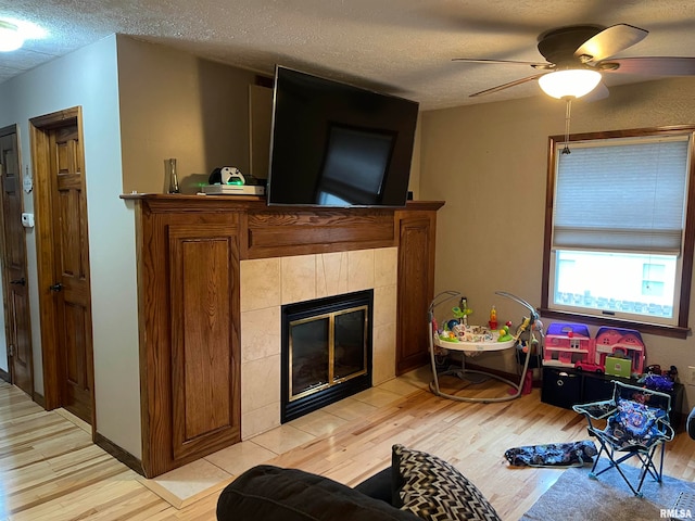 living room with a fireplace, light hardwood / wood-style floors, ceiling fan, and a textured ceiling