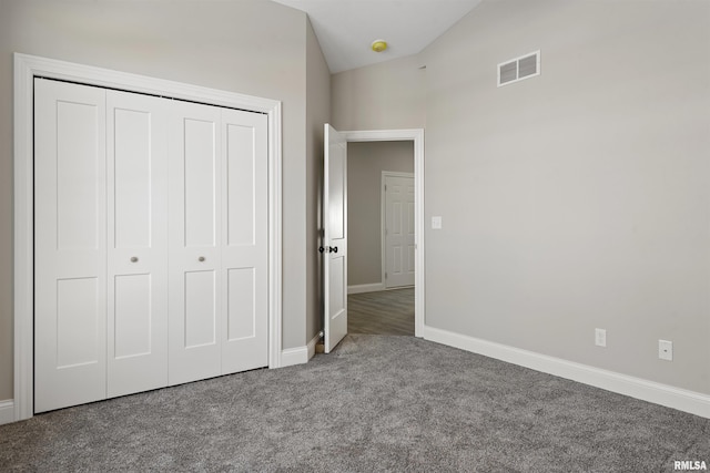 unfurnished bedroom with lofted ceiling, dark carpet, and a closet