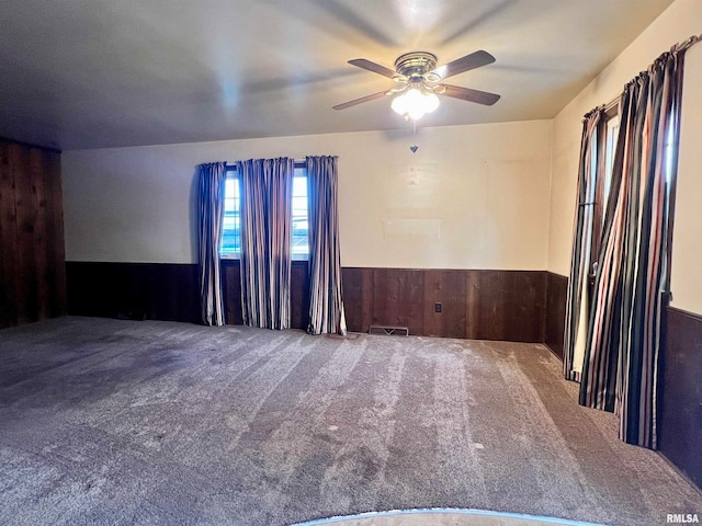 empty room with wood walls, carpet, and ceiling fan