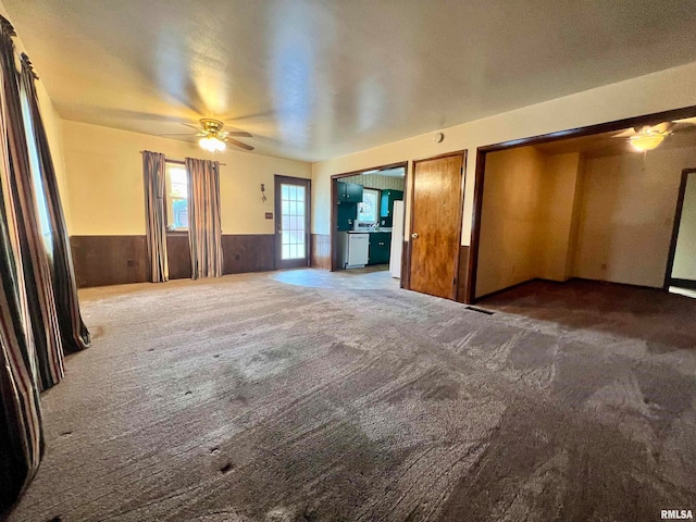 unfurnished living room featuring wooden walls, dark colored carpet, and ceiling fan