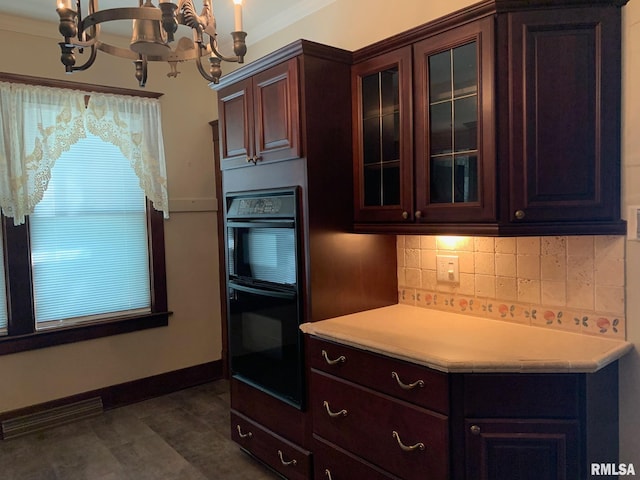 kitchen featuring backsplash, ornamental molding, double oven, dark brown cabinetry, and a chandelier