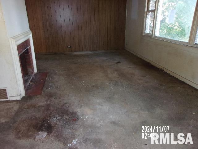 unfurnished living room featuring a brick fireplace and wood walls