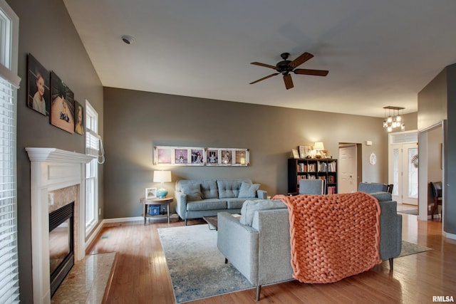 living room featuring ceiling fan with notable chandelier, a high end fireplace, and light hardwood / wood-style flooring