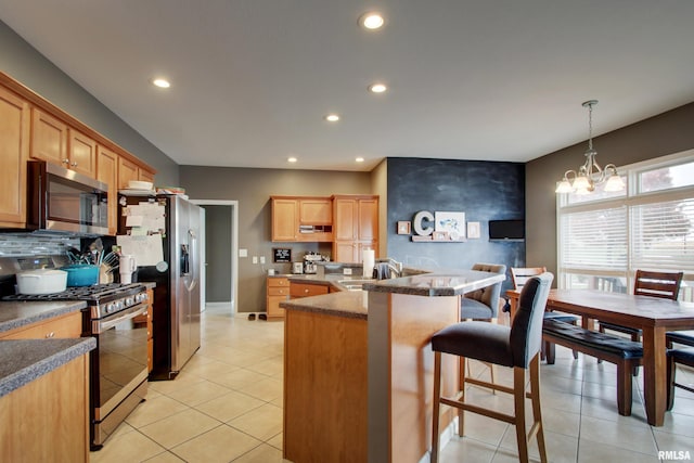 kitchen with tasteful backsplash, appliances with stainless steel finishes, a notable chandelier, a kitchen bar, and hanging light fixtures