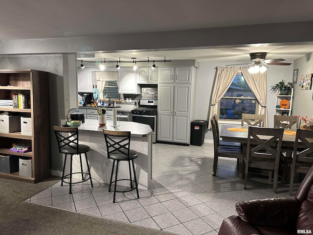 kitchen with decorative backsplash, a breakfast bar area, gas stove, ceiling fan, and white cabinetry