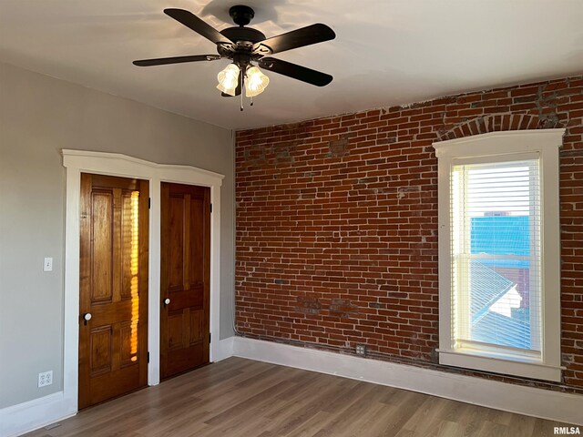 unfurnished room featuring ceiling fan, hardwood / wood-style floors, and brick wall