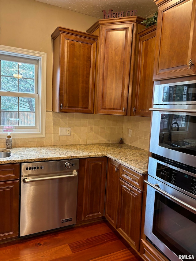 kitchen with dark wood-type flooring, light stone counters, appliances with stainless steel finishes, and tasteful backsplash