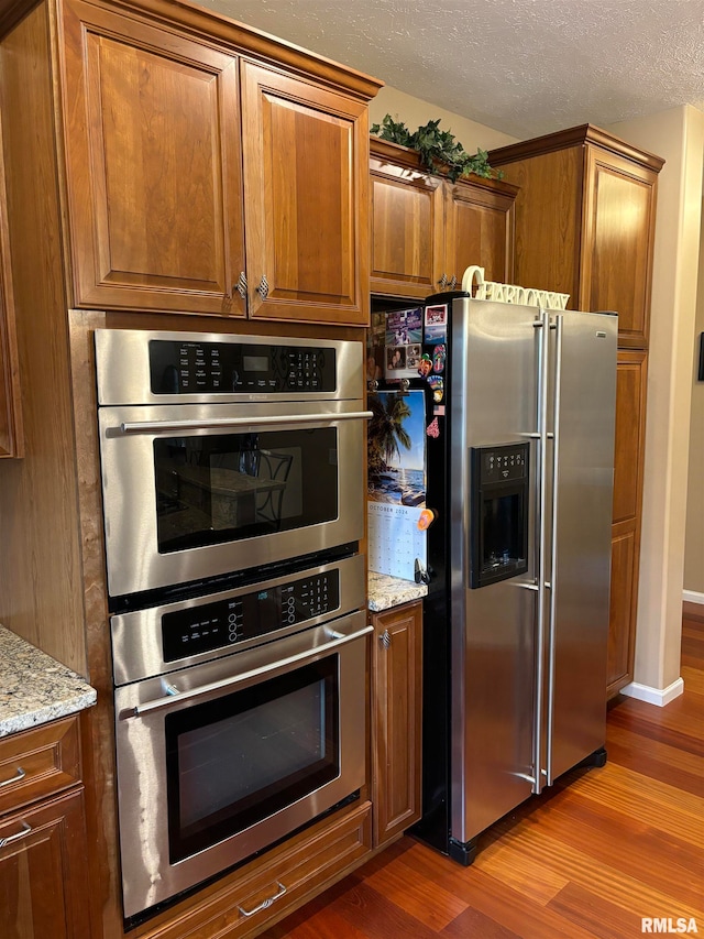 kitchen with light stone countertops, appliances with stainless steel finishes, a textured ceiling, and light wood-type flooring