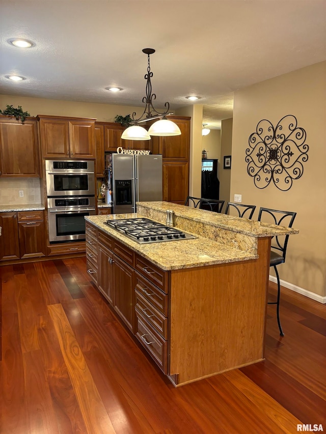 kitchen with stainless steel appliances, light stone countertops, hanging light fixtures, a breakfast bar area, and dark wood-type flooring