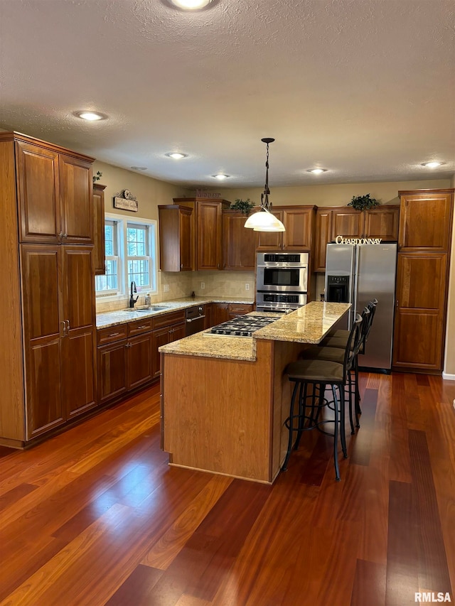 kitchen featuring stainless steel appliances, sink, light stone countertops, a kitchen island, and dark wood-type flooring