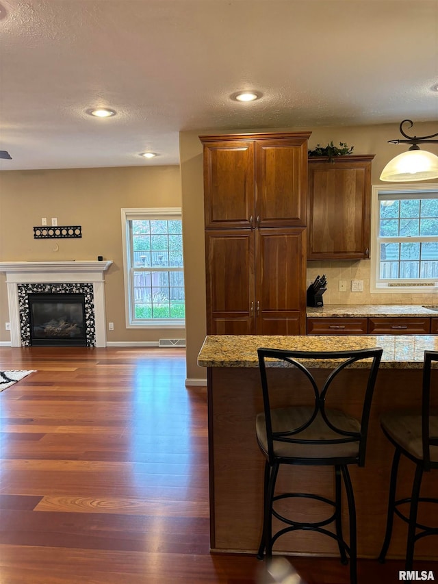kitchen with dark hardwood / wood-style flooring, light stone countertops, a tiled fireplace, and a kitchen bar