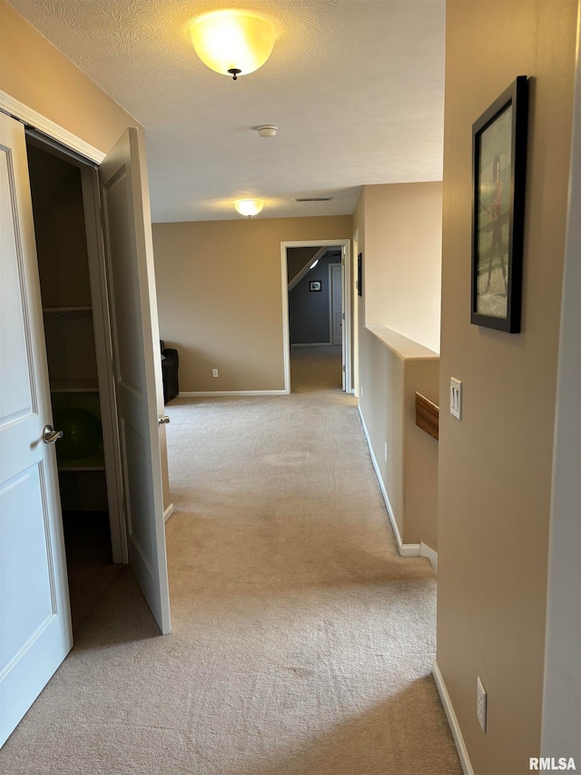 hallway with a textured ceiling and light carpet