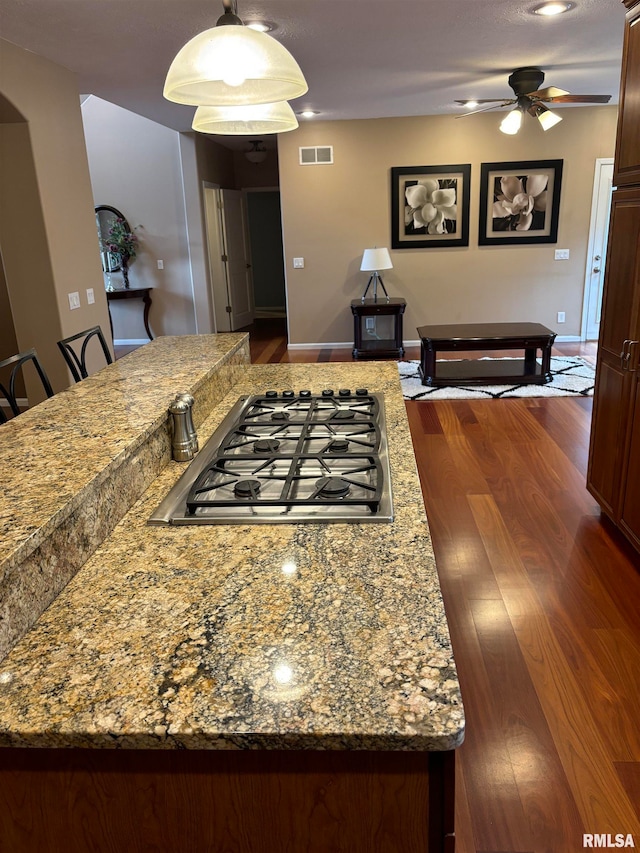 kitchen featuring dark wood-type flooring, stainless steel gas stovetop, light stone counters, ceiling fan, and pendant lighting