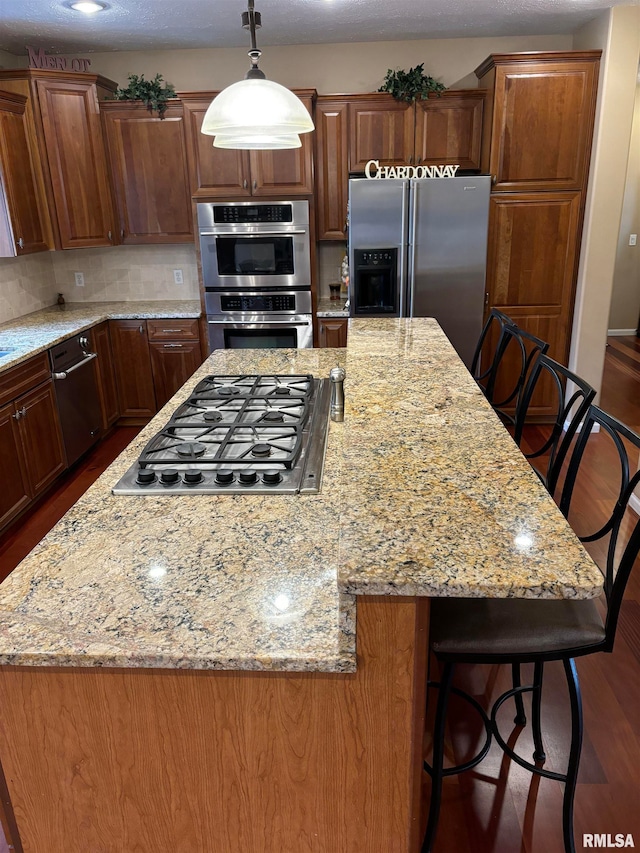 kitchen with appliances with stainless steel finishes, dark hardwood / wood-style floors, backsplash, decorative light fixtures, and a center island
