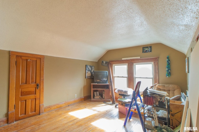 misc room with vaulted ceiling, light hardwood / wood-style floors, and a textured ceiling