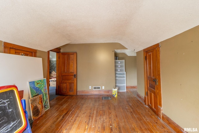 unfurnished living room with vaulted ceiling, wood-type flooring, and a textured ceiling