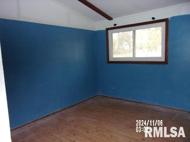 spare room featuring wood-type flooring and vaulted ceiling with beams