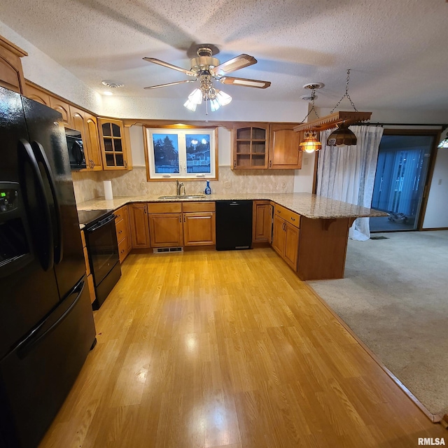 kitchen with kitchen peninsula, light hardwood / wood-style floors, decorative light fixtures, a textured ceiling, and black appliances