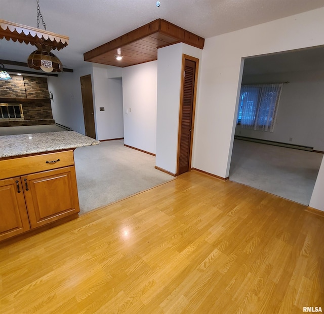 kitchen featuring a brick fireplace, light stone counters, light wood-type flooring, and a baseboard heating unit