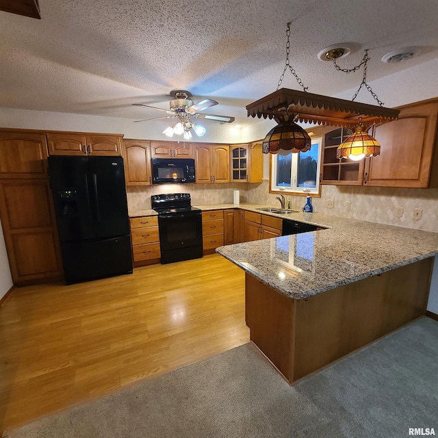 kitchen featuring kitchen peninsula, light wood-type flooring, a textured ceiling, black appliances, and decorative light fixtures