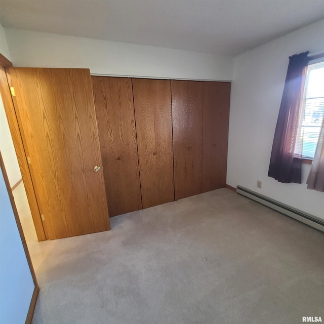 unfurnished bedroom with baseboard heating, light carpet, and a closet