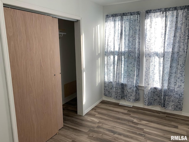 unfurnished bedroom featuring multiple windows, a closet, and dark hardwood / wood-style flooring