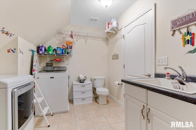 laundry area featuring a textured ceiling, washer and dryer, light tile patterned floors, and sink