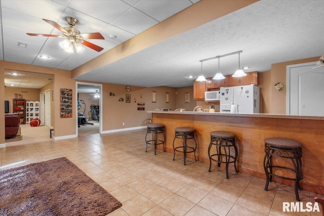 kitchen with ceiling fan, a kitchen bar, white appliances, and light tile patterned floors