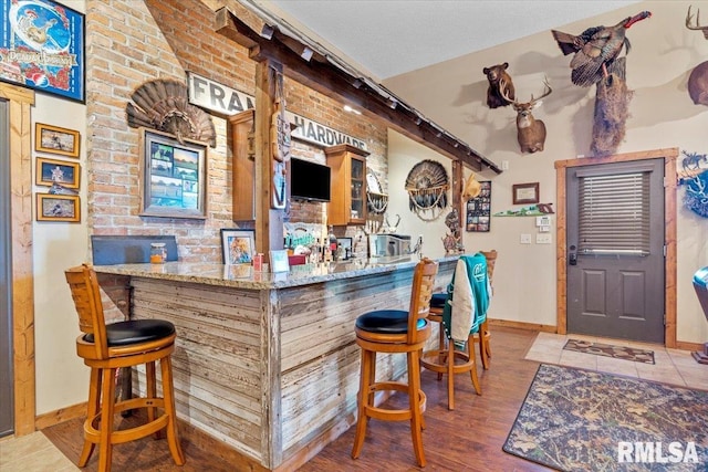 bar featuring a textured ceiling, light wood-type flooring, light stone counters, and brick wall