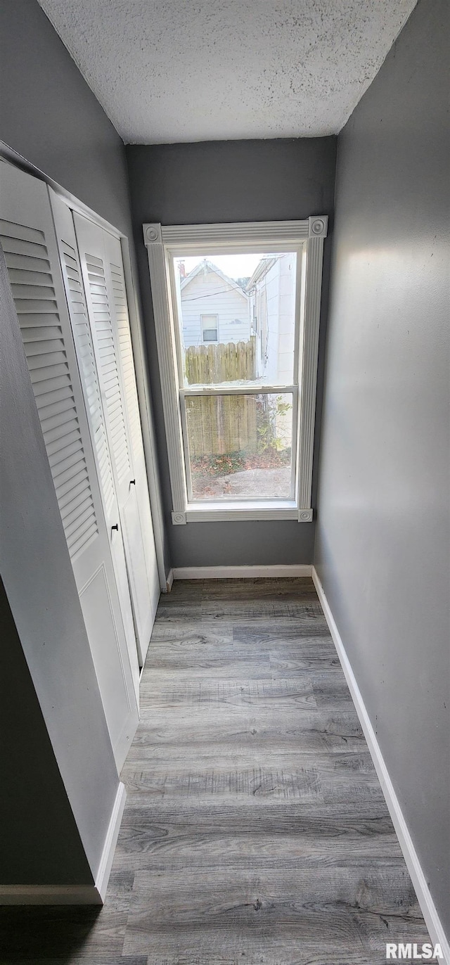 corridor with a textured ceiling and light hardwood / wood-style floors