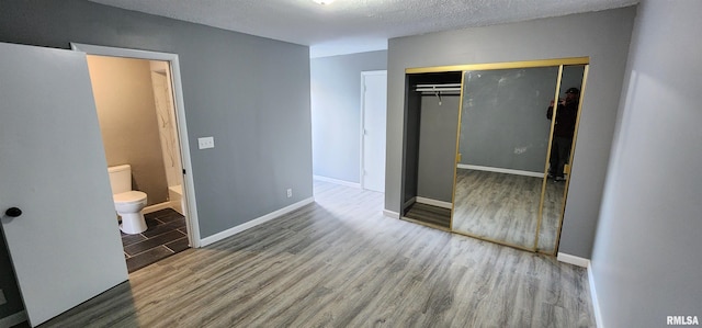 unfurnished bedroom with a textured ceiling, hardwood / wood-style floors, a closet, and ensuite bath