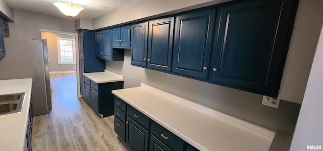 kitchen featuring light wood-type flooring, stainless steel fridge, blue cabinetry, and sink