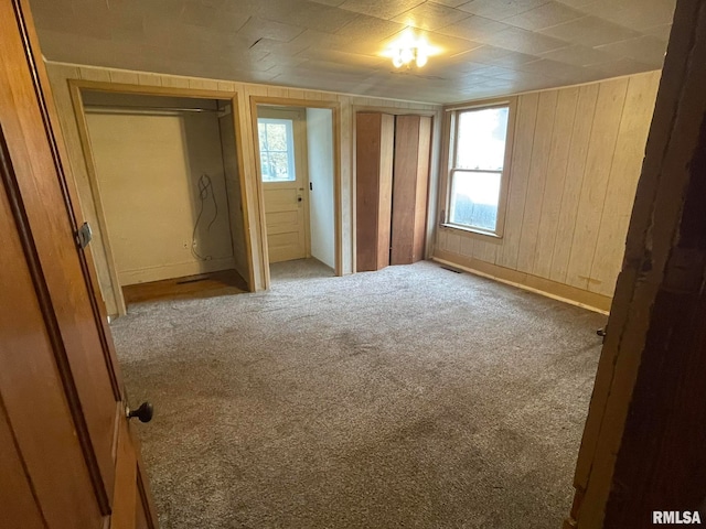 unfurnished bedroom featuring light carpet and wooden walls