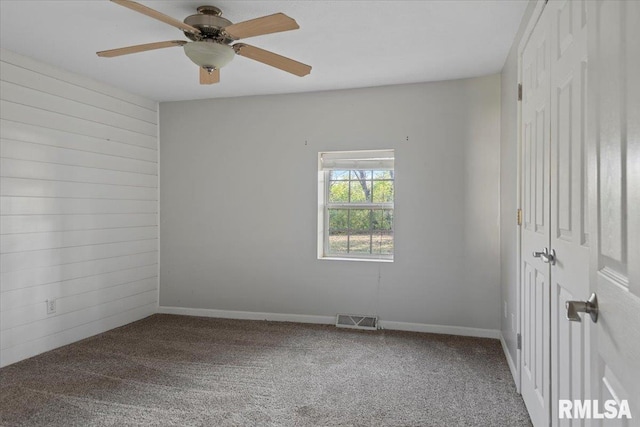 unfurnished room featuring carpet flooring, ceiling fan, and wooden walls