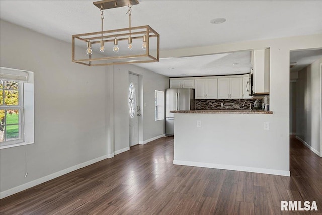 kitchen with kitchen peninsula, backsplash, white cabinetry, dark hardwood / wood-style floors, and stainless steel refrigerator