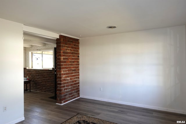 spare room with dark hardwood / wood-style floors and brick wall