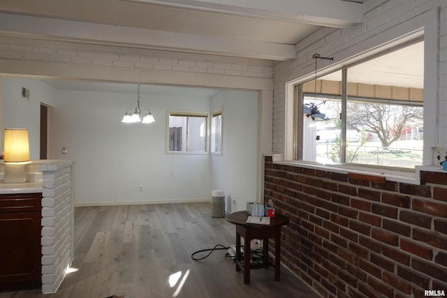 interior space featuring beam ceiling, a chandelier, light hardwood / wood-style flooring, and brick wall