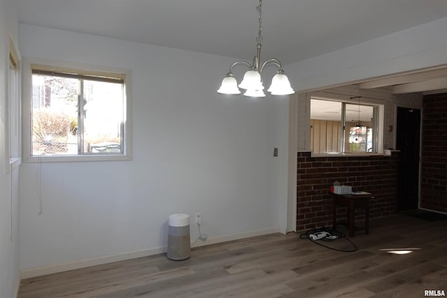 unfurnished dining area with hardwood / wood-style floors, an inviting chandelier, and brick wall