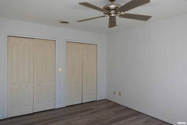 unfurnished bedroom with hardwood / wood-style flooring, ceiling fan, and multiple closets