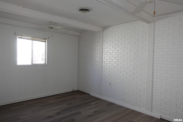 spare room featuring beamed ceiling, dark hardwood / wood-style floors, and brick wall