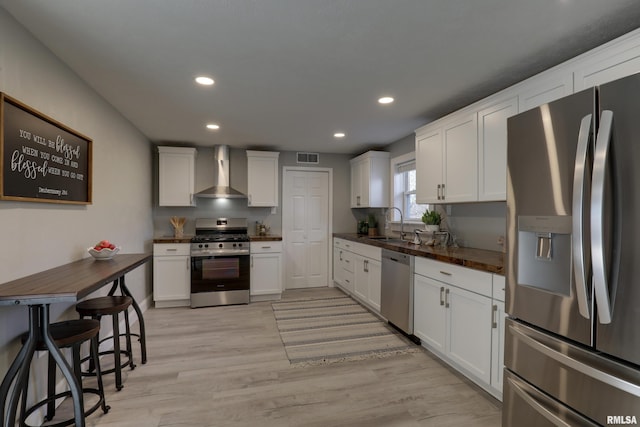 kitchen featuring appliances with stainless steel finishes, dark countertops, white cabinets, and wall chimney exhaust hood