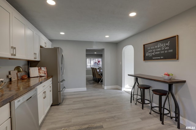 kitchen with light wood finished floors, arched walkways, dishwasher, dark countertops, and white cabinetry