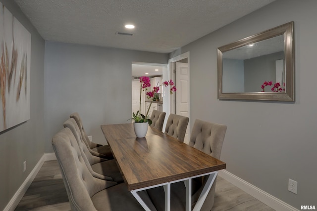 dining room with a textured ceiling, baseboards, and wood finished floors