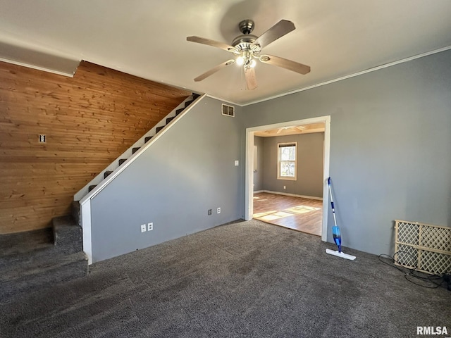 interior space featuring wood walls, ceiling fan, and dark carpet