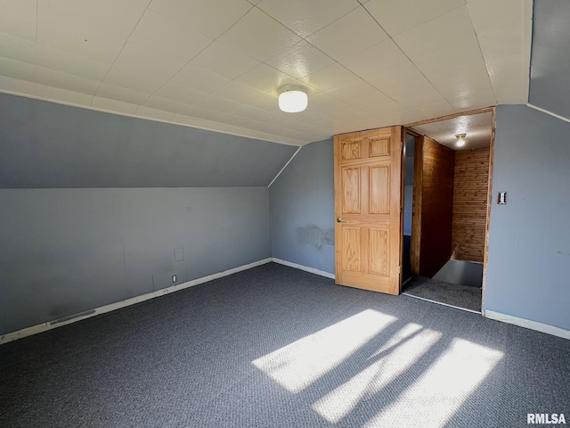 additional living space with wooden walls, lofted ceiling, and dark colored carpet