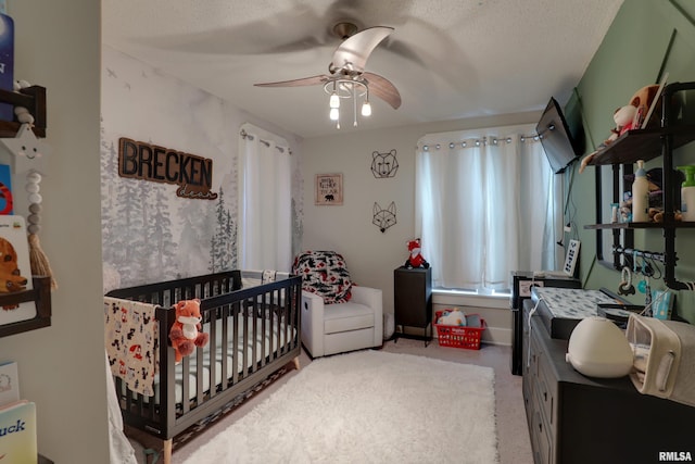 bedroom with ceiling fan, light colored carpet, a textured ceiling, and a nursery area