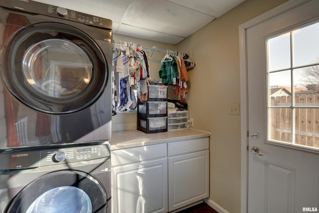 clothes washing area with stacked washer and dryer and cabinets